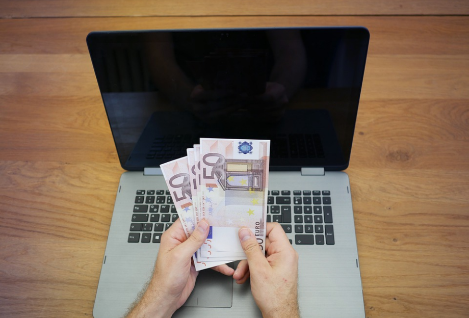 a person holding money in front of a laptop
